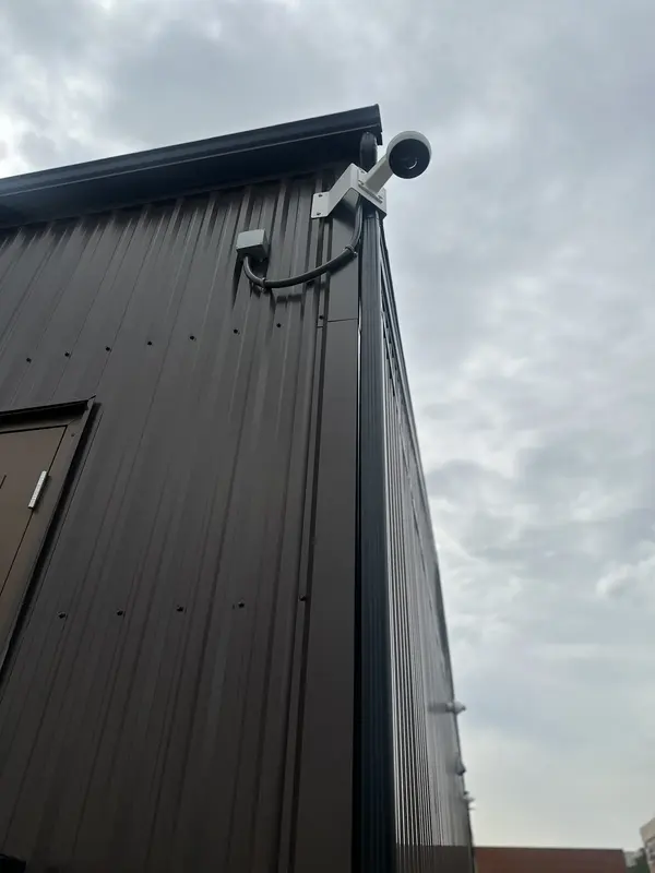 Exterior security camera mounted at the roofline of a metal-clad commercial building