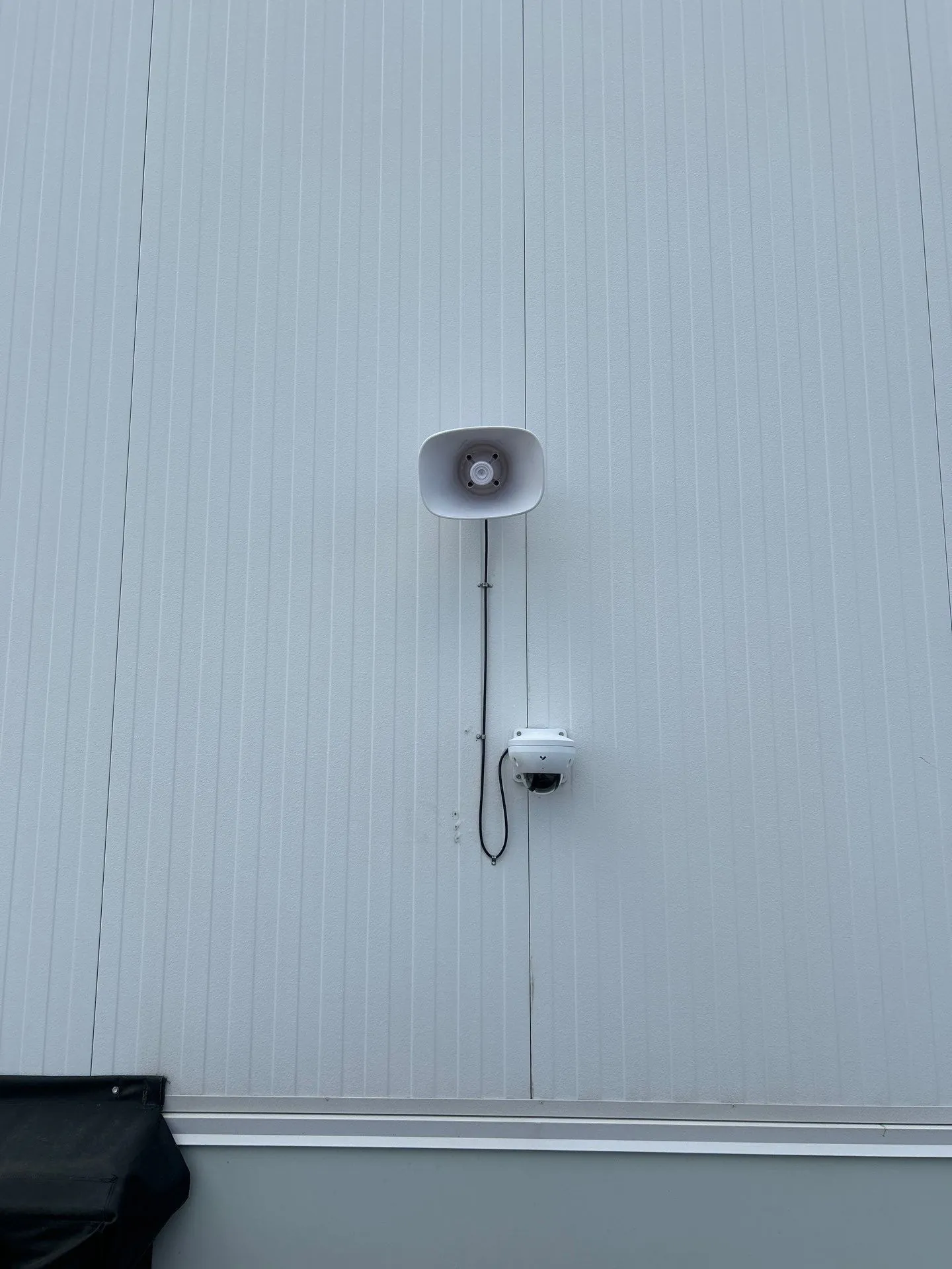 Outdoor speaker and mini dome security camera mounted on an industrial building exterior wall