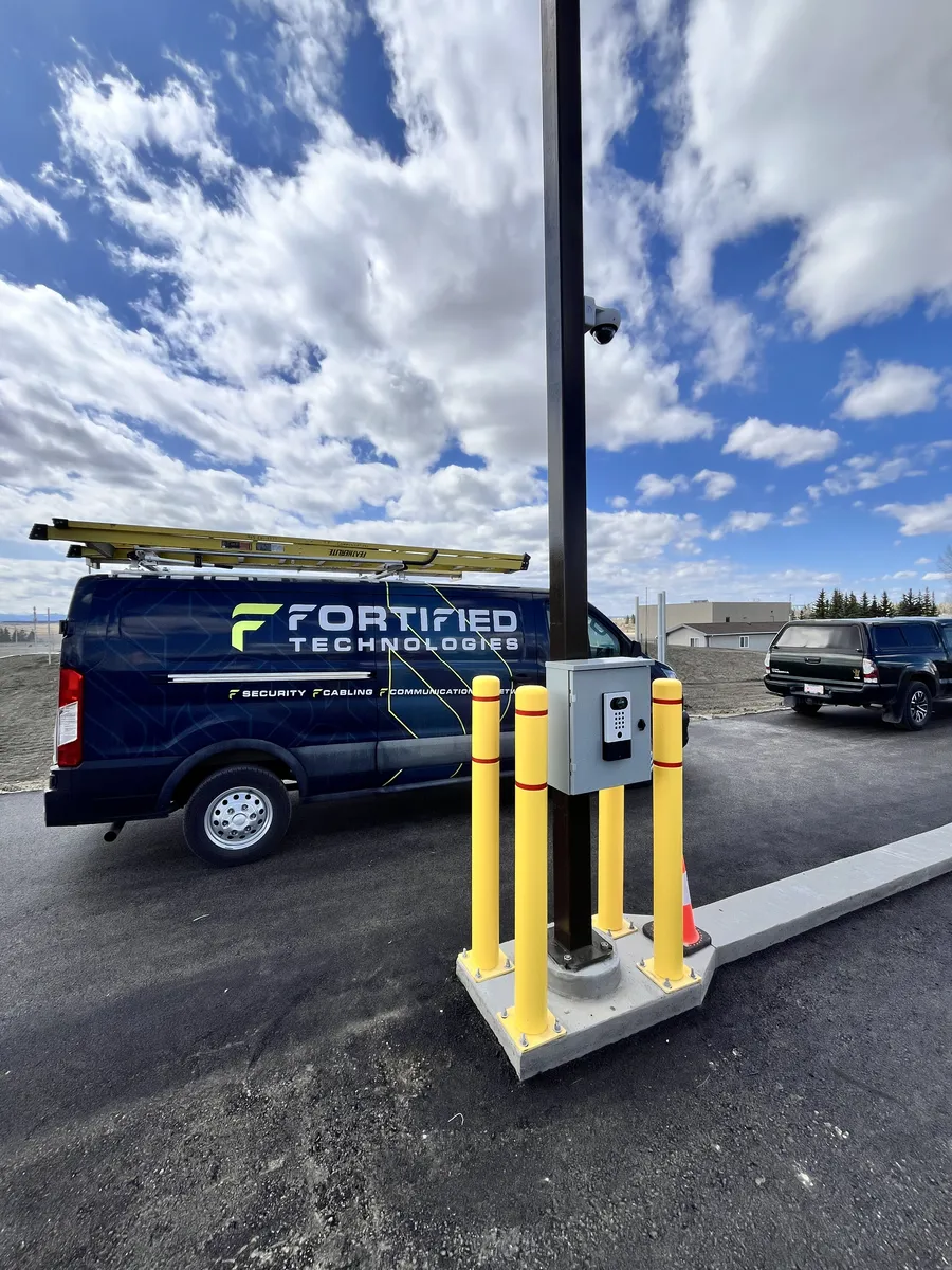 Security camera and access control panel installed on a parking lot light pole with a Fortified Technologies van nearby