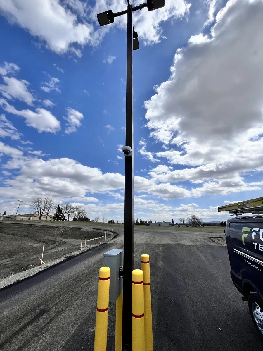 Security camera mounted high on a light pole overlooking a commercial parking lot construction site