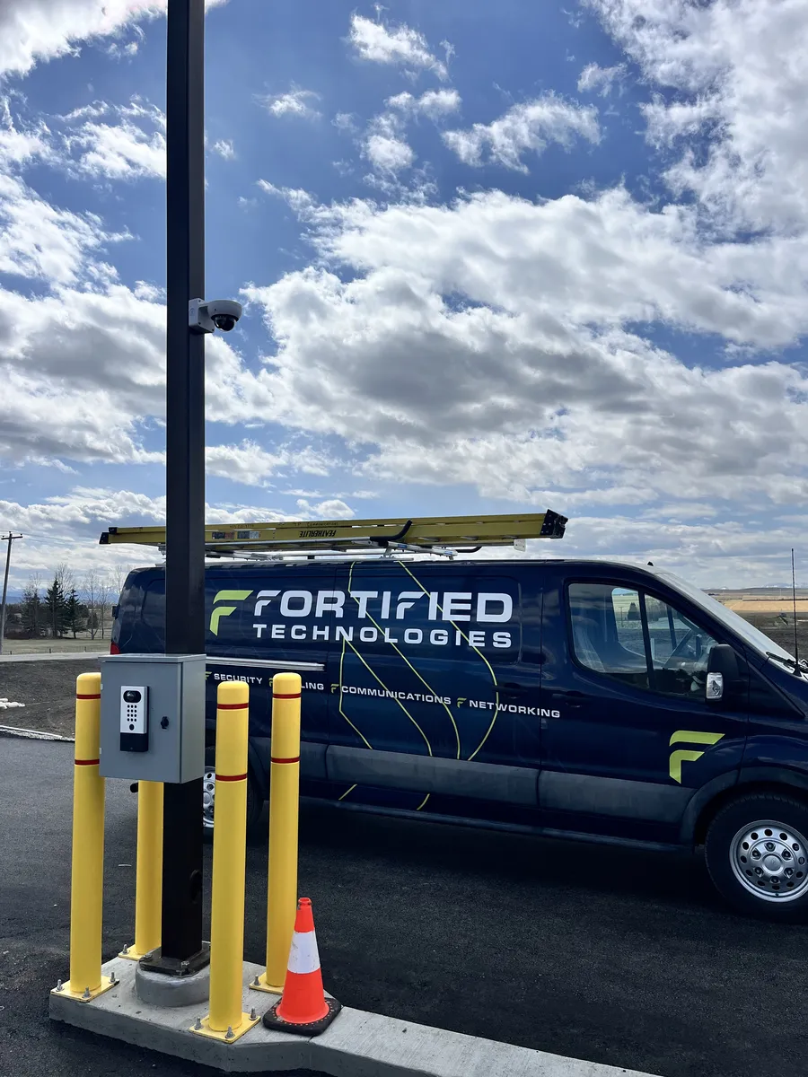 Security camera and access control panel on a parking lot light pole with a Fortified Technologies service van in the background