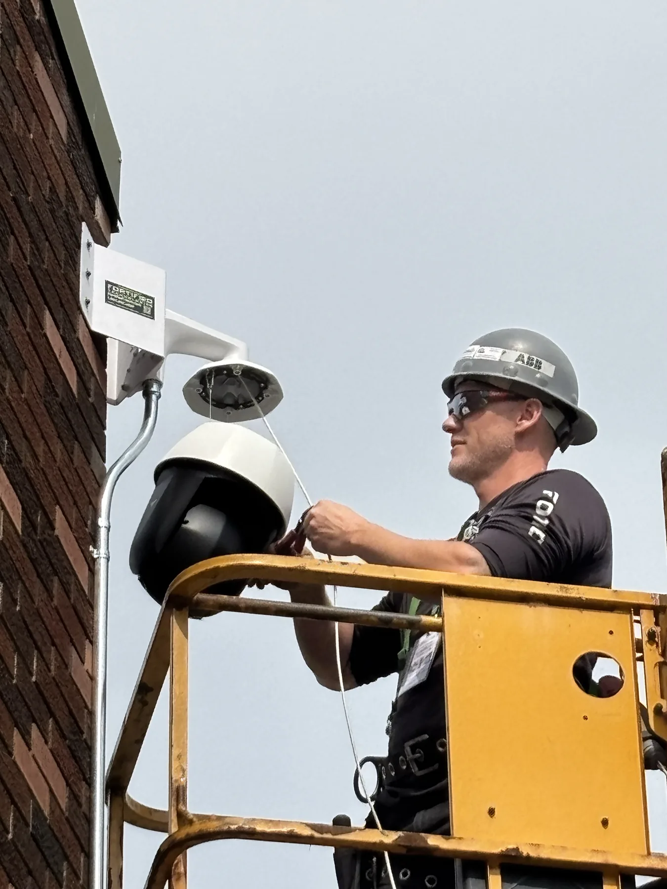 Technician in an elevated work platform installing security equipment on a brick commercial building