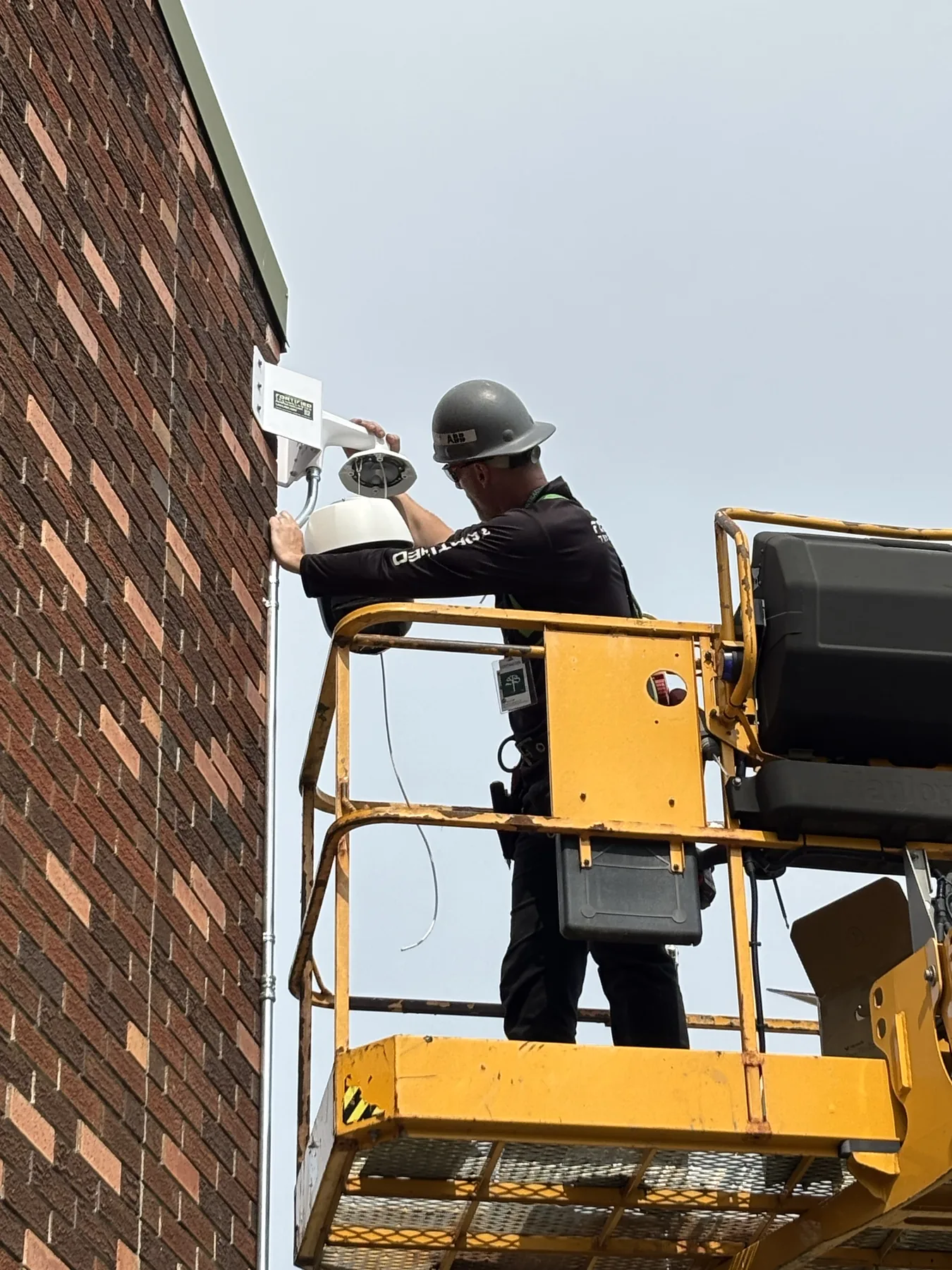 Technician working from an elevated platform on a brick building security camera installation