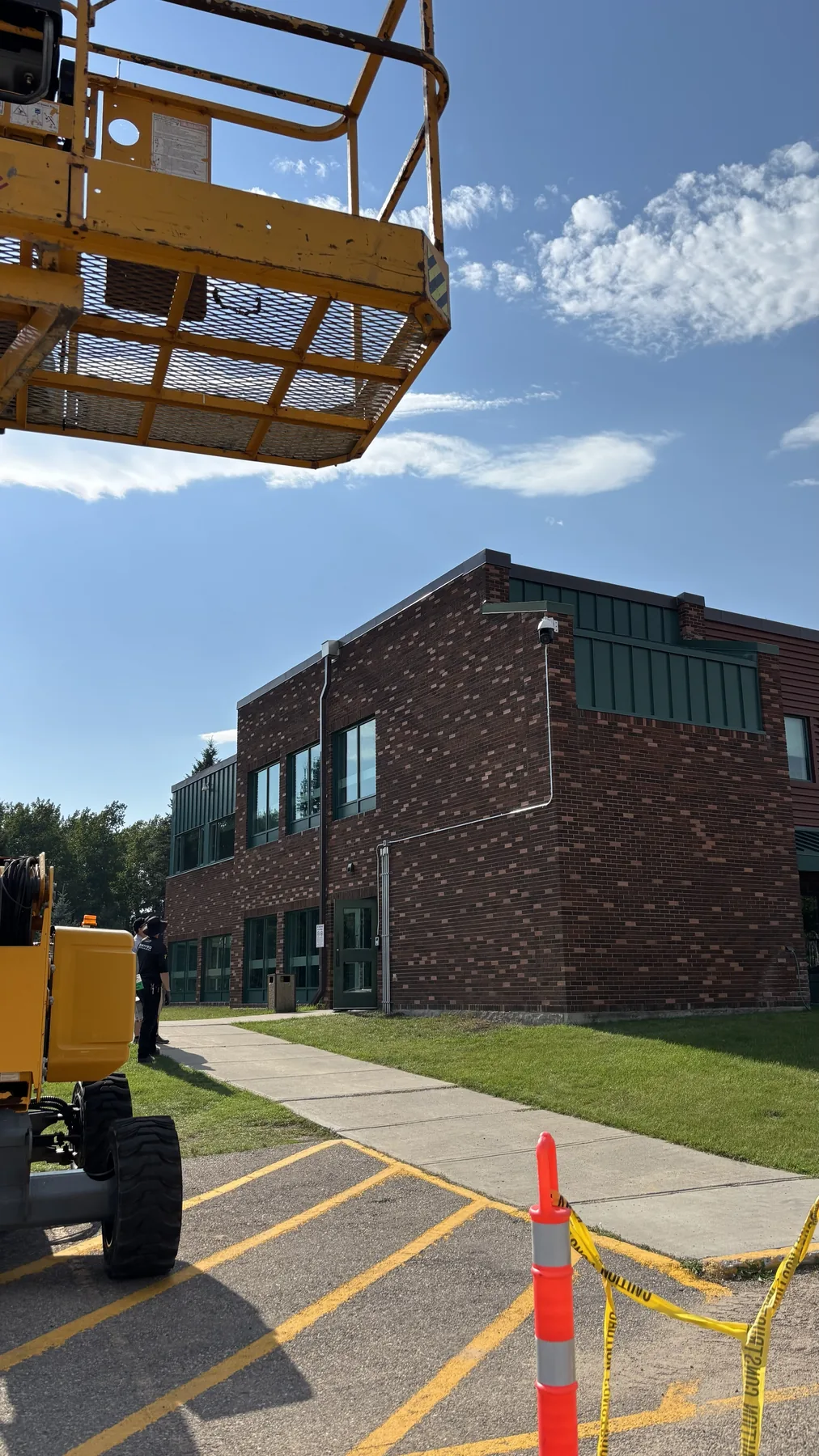 Elevated work platform positioned beside a brick commercial building during a security camera installation